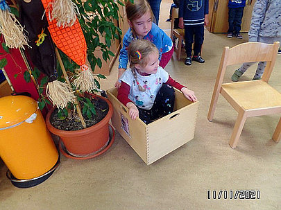 Ein Kind schiebt ein anderes in einer Holzbox umher