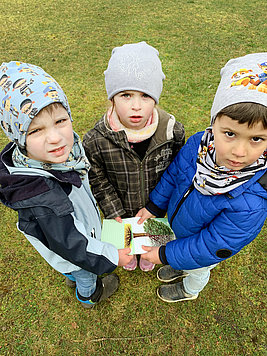 Drei Kinder halten eine Baumkarte in die Kamera