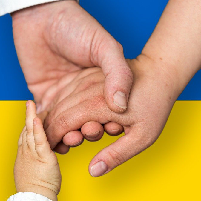Eine Familie hält sich bei den Händen. Im Hintergrund die Ukrainische Flagge.