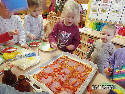 Mehrere Kinder backen gemeinsam eine Pizza