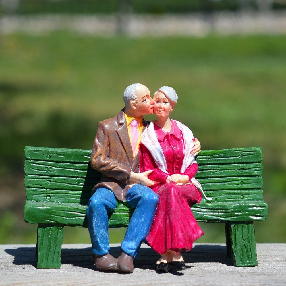 Figuren eines älteren Pärchens, die sich umarmend auf einer Bank sitzen