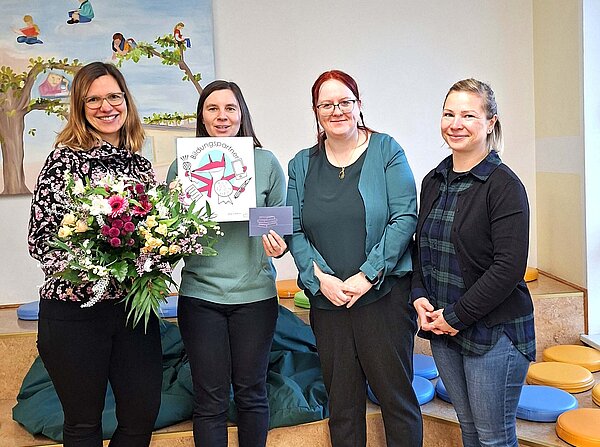 Mitarbeiterinnen, die gemeinsam eine Auszeichnung und einen Blumenstrauß halten.