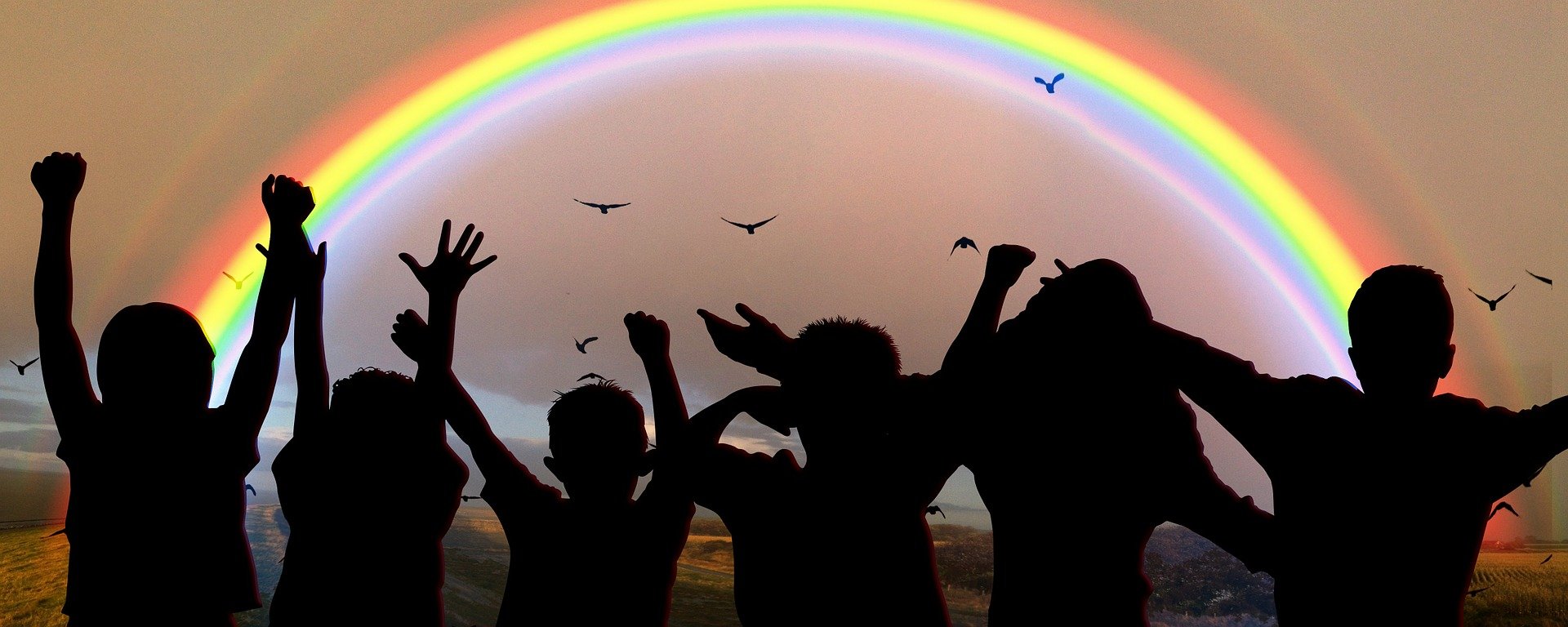 Silhouetten von Kindern, die vor einem Regenbogen stehen